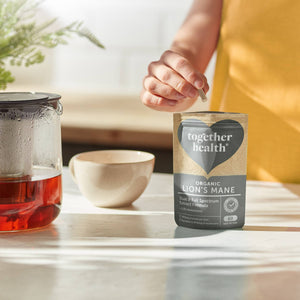 Together Health organic lion's mane supplement on a table with a glass of tea and a bowl.