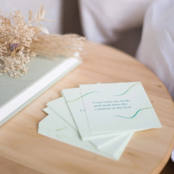 Sleep affirmation cards laid on a wooden table beside a journal, simple prompts for mindful reflection as part of bedtime routine.

